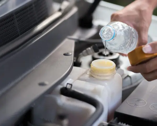 Mani versano acqua distillata nel serbatoio del radiatore dell'auto, un gesto di cura per il motore.
