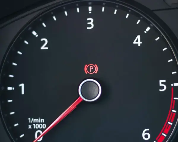 Cruscotto auto con tachimetro e spia freno a mano accesa.