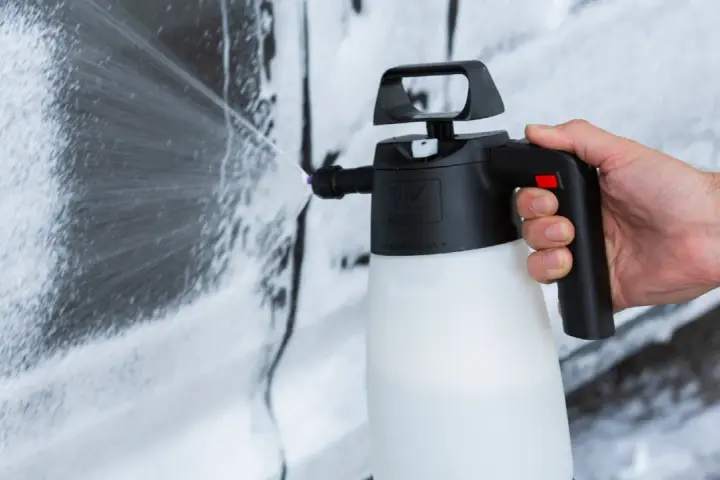 Mano che spruzza schiuma per lavare auto a casa con un erogatore.