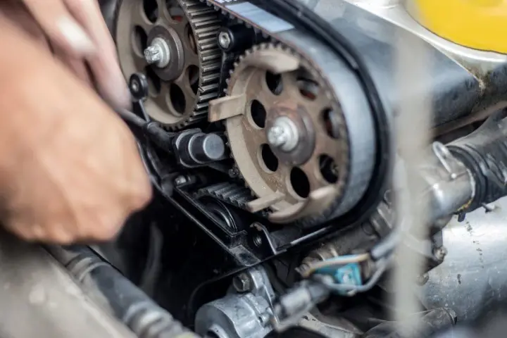 Mano che lavora sul motore, ingranaggi e cinghia di distribuzione. Scopri quanto costa cambiare la cinghia di distribuzione per la tua auto.