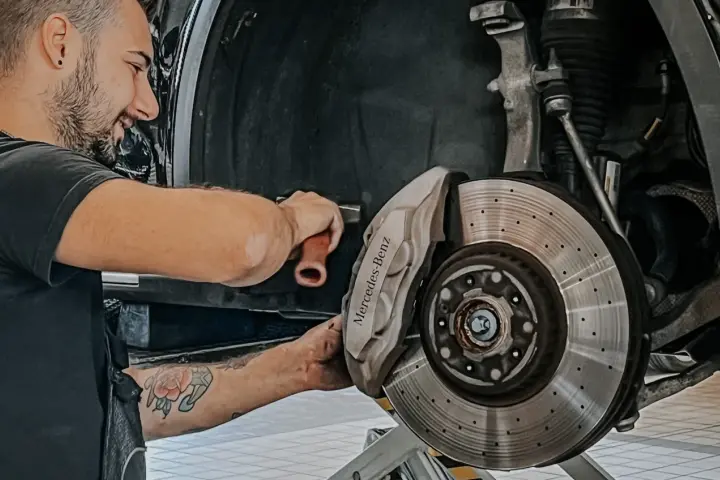 Meccanico sorridente effettua manutenzione a3 Mercedes, concentrato sul freno a disco forato e pinza con logo.