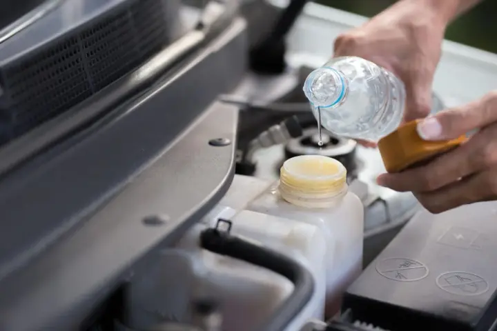 Mani versano acqua distillata nel serbatoio del radiatore dell'auto, un gesto di cura per il motore.
