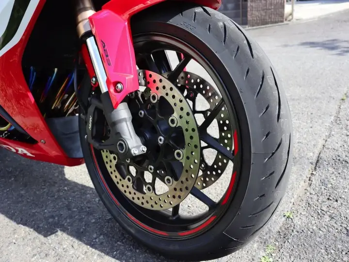 Ruota anteriore di una moto rossa, con disco freno forato e pinza ABS. Il volante che vibra a bassa velocità è un dettaglio che si percepisce.