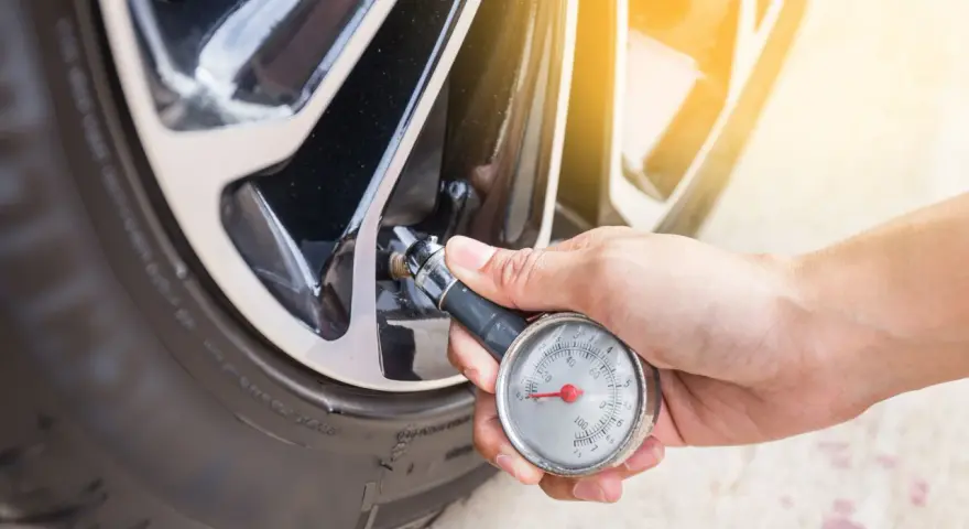 Controllo della pressione gomme auto con manometro. La mano tiene lo strumento collegato alla valvola del pneumatico.