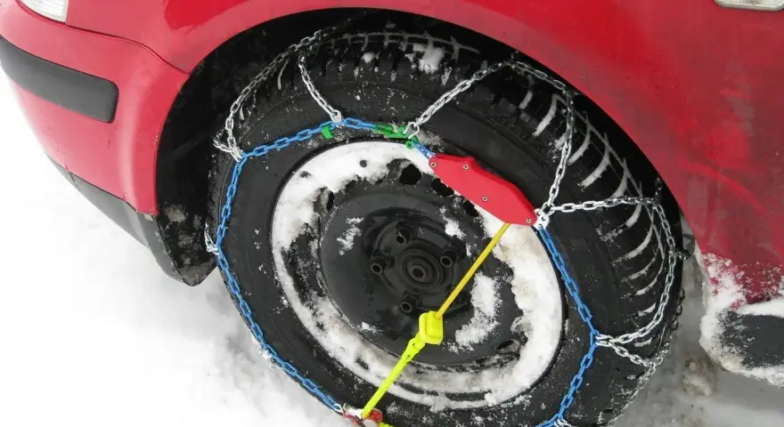 Ecco come mettere le catene da neve: una ruota di un'auto rossa coperta di neve con catene montate.