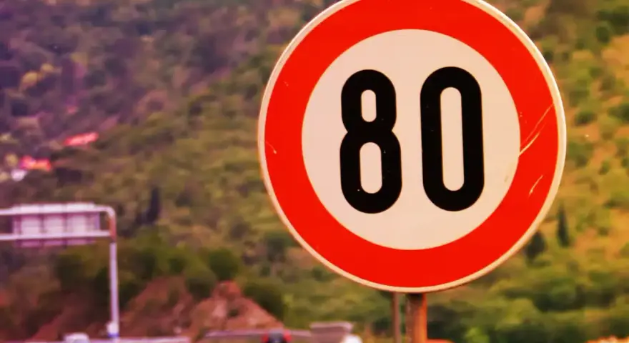 Segnale di limite massimo nei centri abitati: 80 km/h. Strada panoramica con vegetazione sullo sfondo.