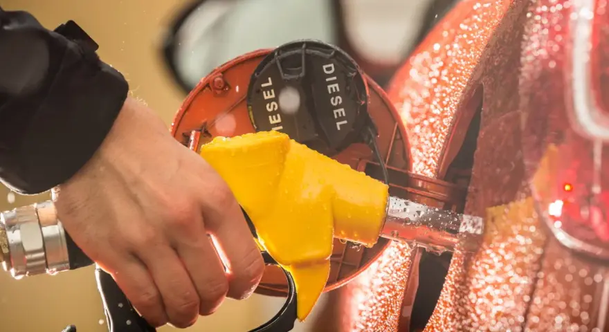 Mano che inserisce la pompa del **diesel nella benzina**. Gocce d'acqua sulla carrozzeria arancione.