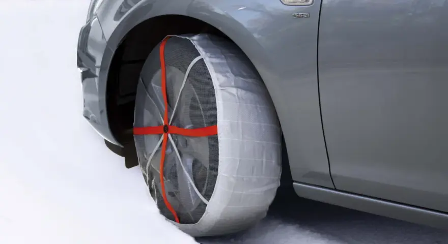 Calze da neve omologate in Italia montate su un'auto grigia su strada innevata.