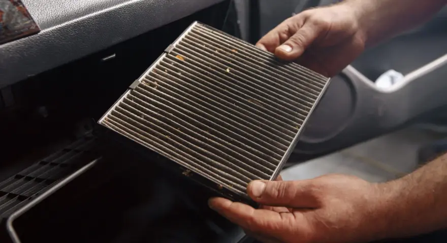 Mani che estraggono un filtro abitacolo sporco, suggerendo la necessità di cambiarlo.