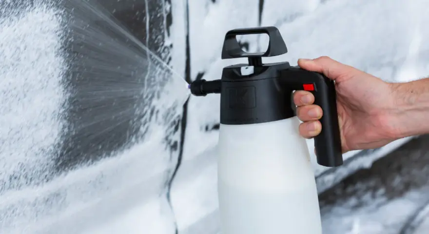 Mano che spruzza schiuma per lavare auto a casa con un erogatore.