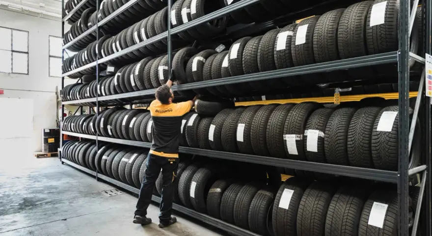 Un uomo in magazzino controlla il deposito pneumatici. Scaffali pieni di gomme, pronte per essere montate.