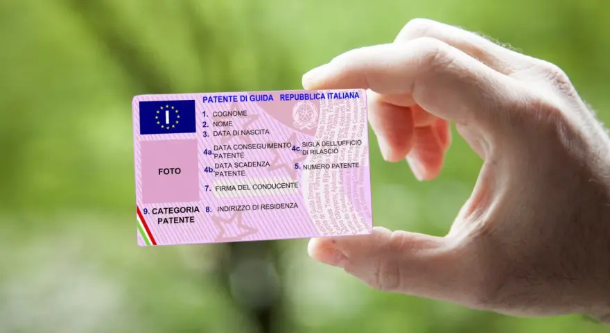 Mano che tiene una patente italiana, con dettagli su nome, data di nascita e scadenza. Nuove regole patente in arrivo?