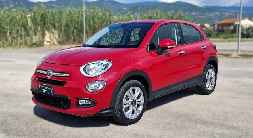 Fiat 500X rossa parcheggiata all'aperto, con montagne sullo sfondo. Controlla la pressione pneumatici per un viaggio sicuro.