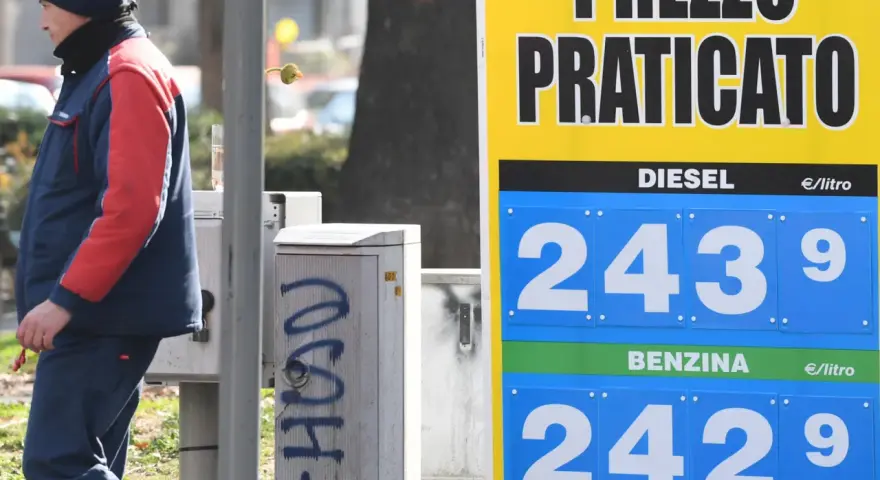 Prezzo praticato per la benzina: 2,429 €/litro. Un uomo in divisa osserva il cartello.