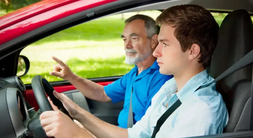 Un giovane neopatentato al volante, con un accompagnatore anziano che indica la strada.