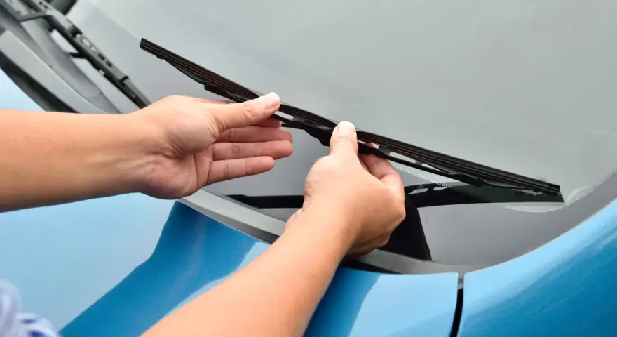 Mani che sostituiscono un tergicristallo sul parabrezza di un'auto blu. Guida rapida su come cambiare tergicristalli.