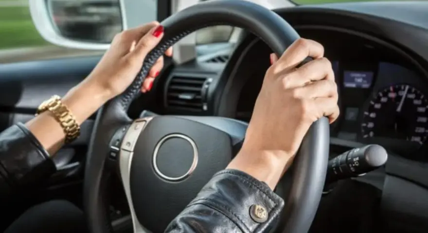 Mani con smalto rosso e bracciale d'oro tengono il volante. Il cruscotto mostra la velocità, definendo cosa vuol dire anteriore in un'auto.