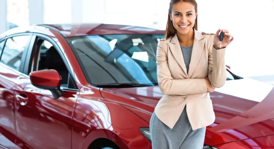Donna sorridente con le chiavi in mano, accanto a una nuova auto rossa, pronta per il rodaggio.