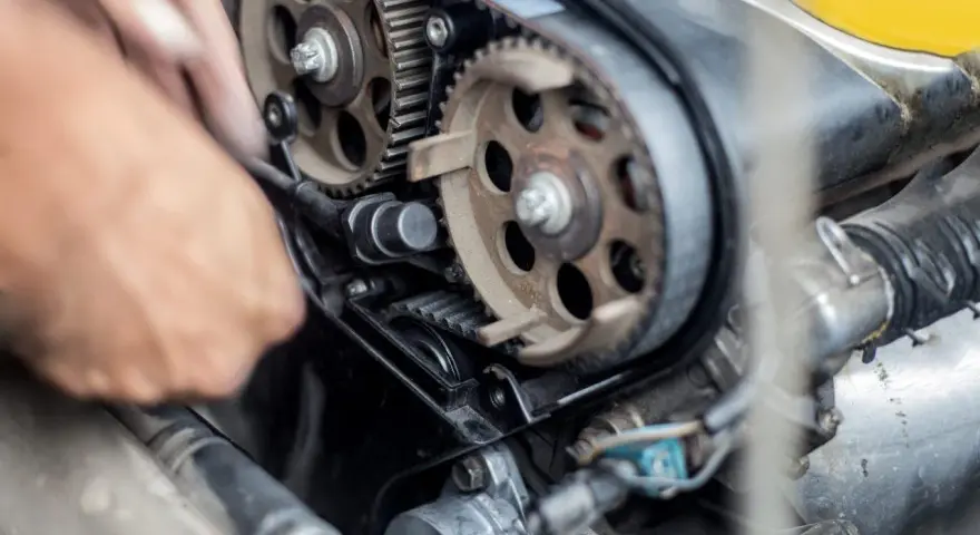 Mano che lavora sul motore, ingranaggi e cinghia di distribuzione. Scopri quanto costa cambiare la cinghia di distribuzione per la tua auto.