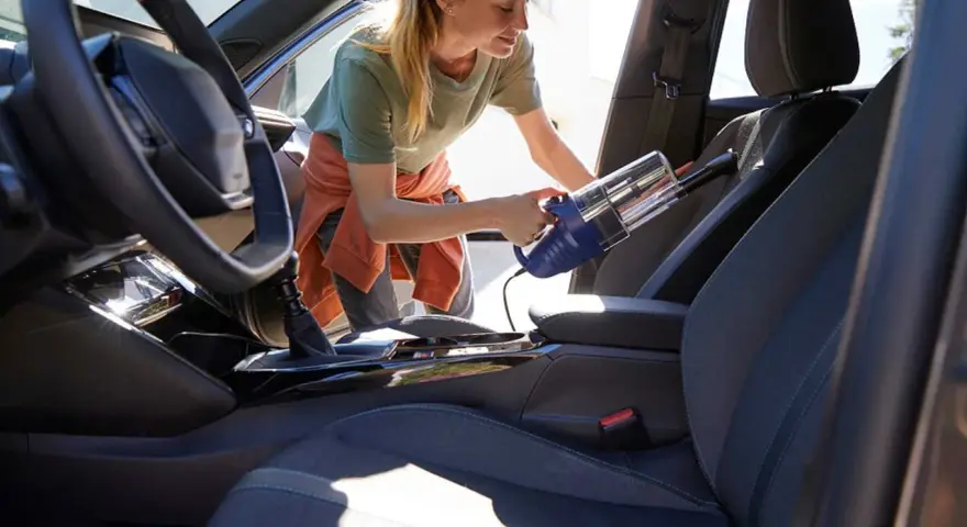Donna usa un aspirapolvere portatile per pulire i sedili dell'auto, rimuovendo polvere e briciole per un interno impeccabile.