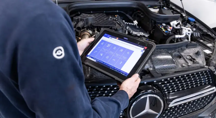 Meccanico usa tablet per diagnosi auto. Il display mostra icone per controlli e manutenzione, suggerendo quanto dura la revisione auto.