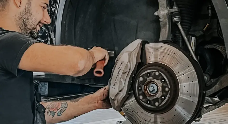 Meccanico sorridente effettua manutenzione a3 Mercedes, concentrato sul freno a disco forato e pinza con logo.