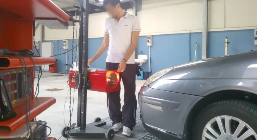 Tecnico effettua la revisione auto ibride in officina, regolando un faro con apparecchiatura specifica.