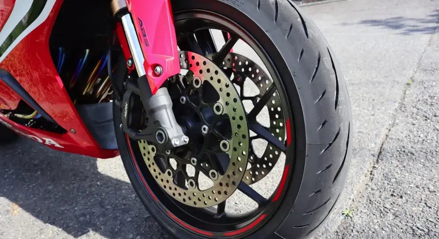 Ruota anteriore di una moto rossa, con disco freno forato e pinza ABS. Il volante che vibra a bassa velocità è un dettaglio che si percepisce.