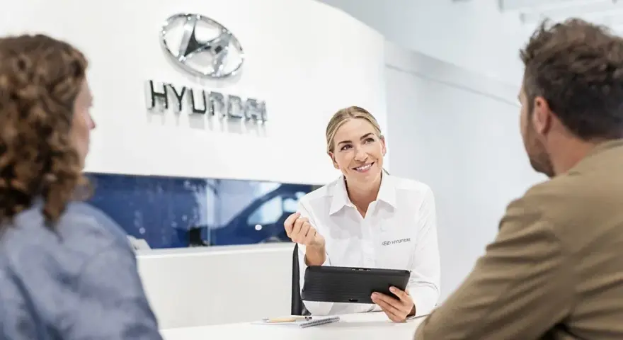 Venditrice Hyundai sorridente mostra un tablet a una coppia, discutendo il tagliando della loro auto.