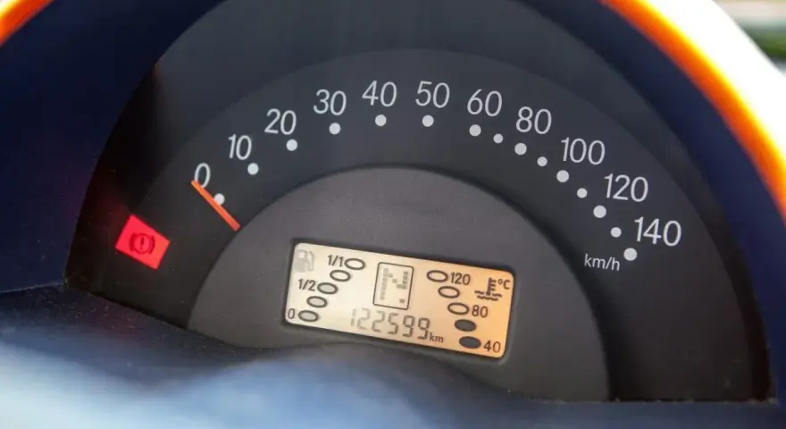 Cruscotto auto con tachimetro e spia del freno di stazionamento accesa. Chilometraggio 122599 km.