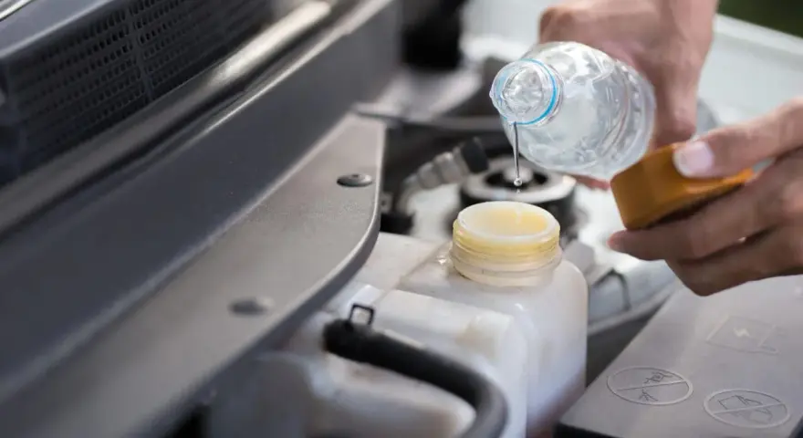 Mani versano acqua distillata nel serbatoio del radiatore dell'auto, un gesto di cura per il motore.