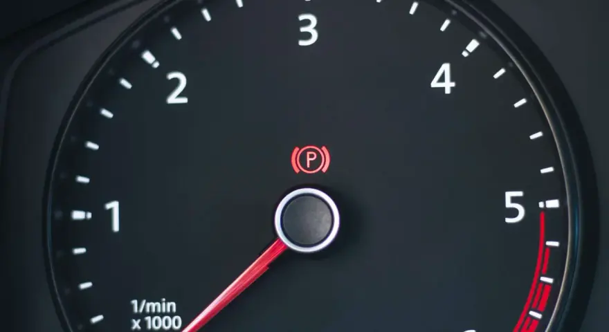 Cruscotto auto con tachimetro e spia freno a mano accesa.