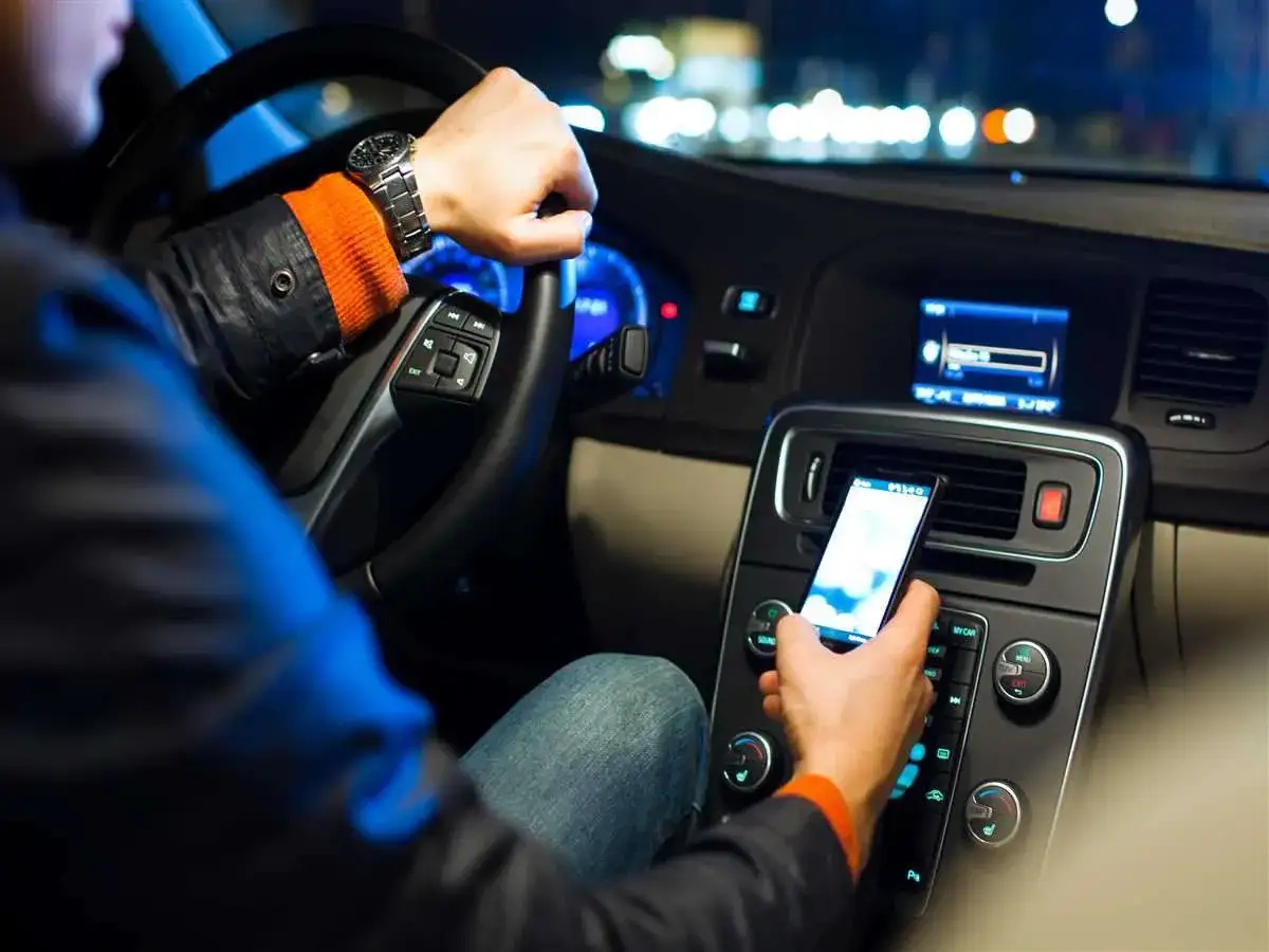 Uomo al volante usa il cellulare, distraendosi dalla guida notturna.