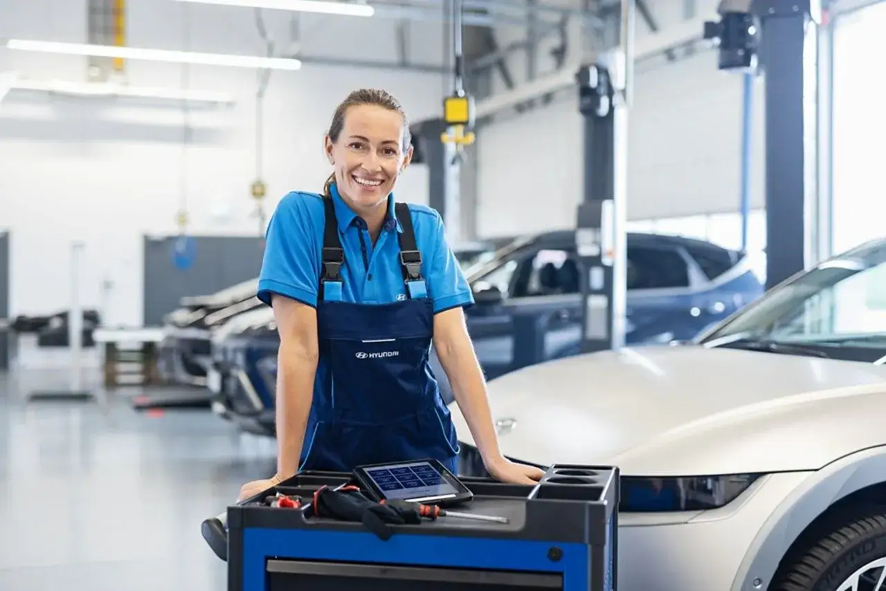 Tecnica sorridente in officina, pronta per il tagliando Hyundai. Sul carrello, tablet e attrezzi.