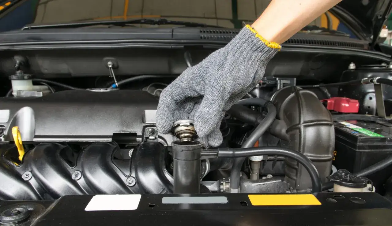 Mano guantata che controlla il tappo del radiatore, assicurandosi che l'acqua distillata sia al livello corretto per il motore.