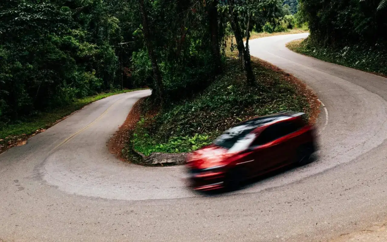 Auto rossa in curva su strada tortuosa, il freno motore aiuta a controllare la discesa.