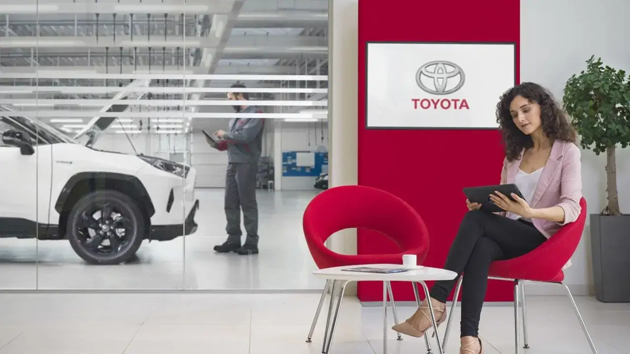 Cliente attende in sala d'attesa Toyota mentre un tecnico controlla un'auto. Scopri il tagliando Toyota prezzo.