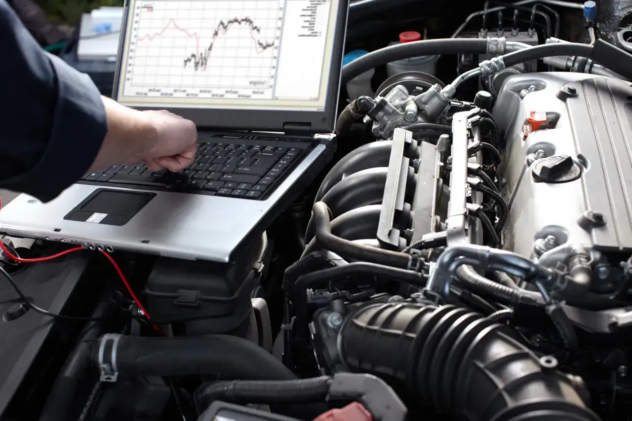 Un tecnico analizza i dati della centralina elettronica di un'auto su un laptop, con il motore in primo piano.