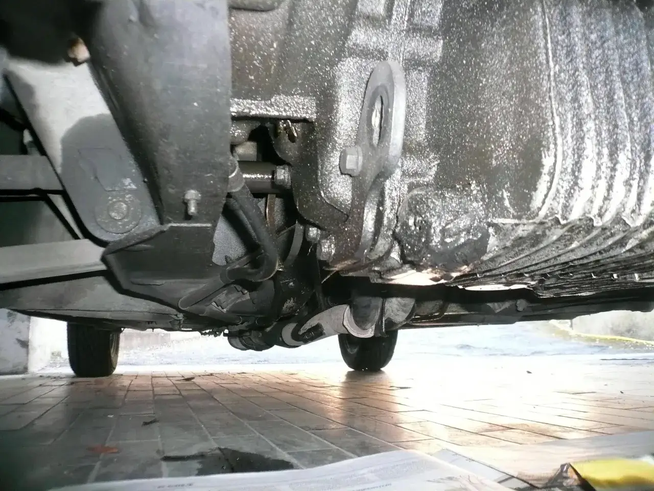 Sotto un'auto, si vede la coppa dell'olio rotta con perdite visibili. I sintomi di una coppa dell'olio rotta includono macchie d'olio sotto il veicolo.