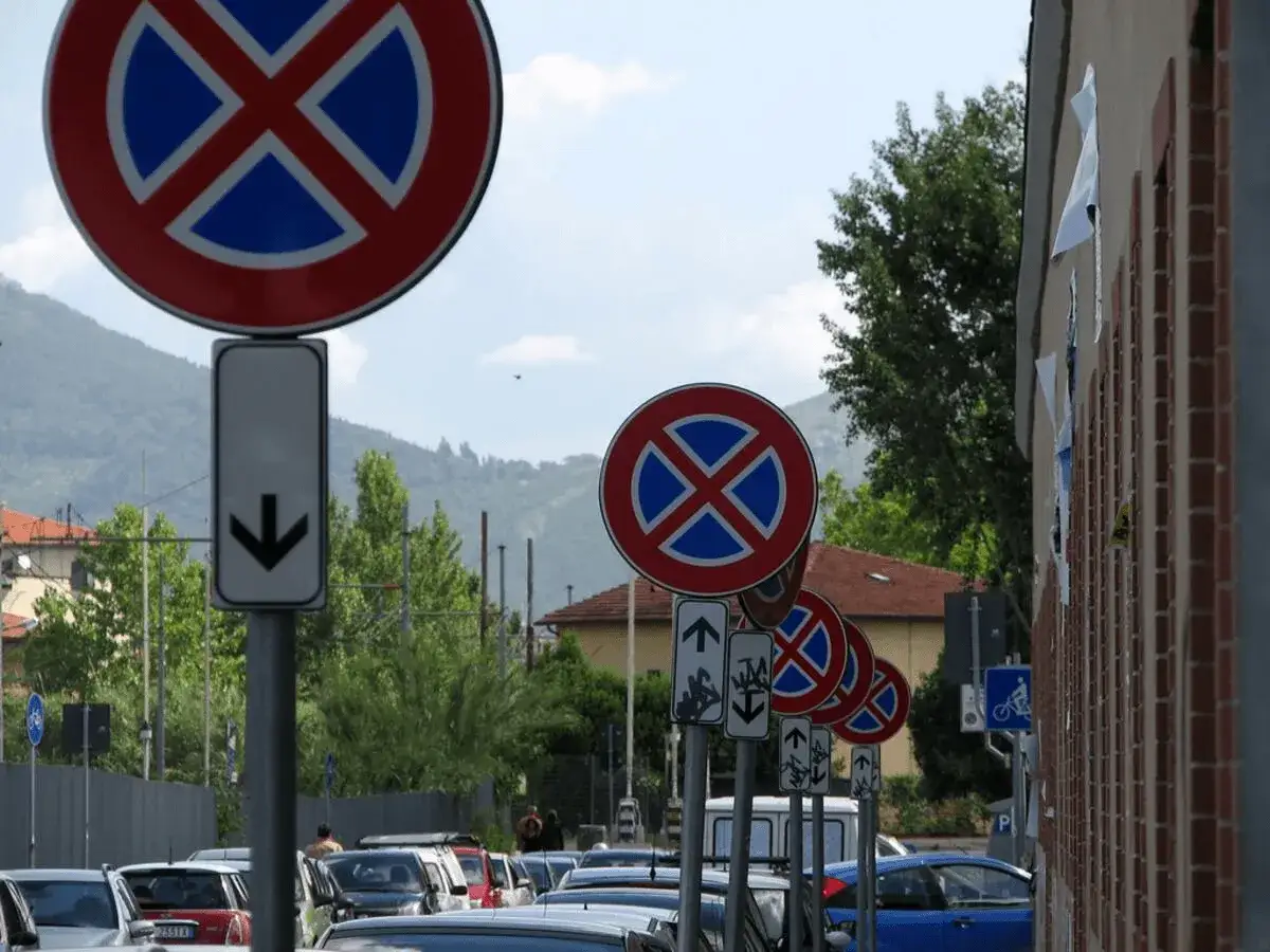 Numerosi cartelli stradali con il significato di divieto di sosta e fermata, alcuni con frecce direzionali, in una strada trafficata.
