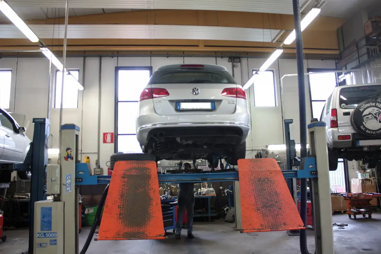 Officina con auto sollevate per controllo assetto ruote. Meccanico al lavoro sotto un'auto.