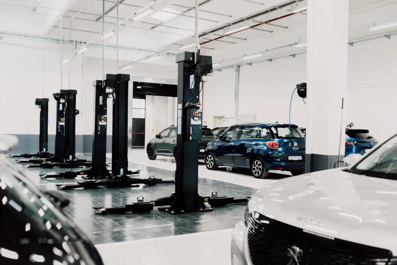 Officina moderna con ponti sollevatori pronti per la manutenzione auto. Diverse auto attendono il loro turno per controlli e riparazioni.