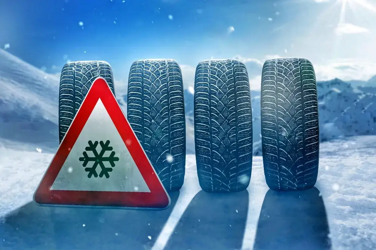 Quattro pneumatici invernali su tutte le ruote, pronti ad affrontare la neve, con un segnale di pericolo fiocco di neve.