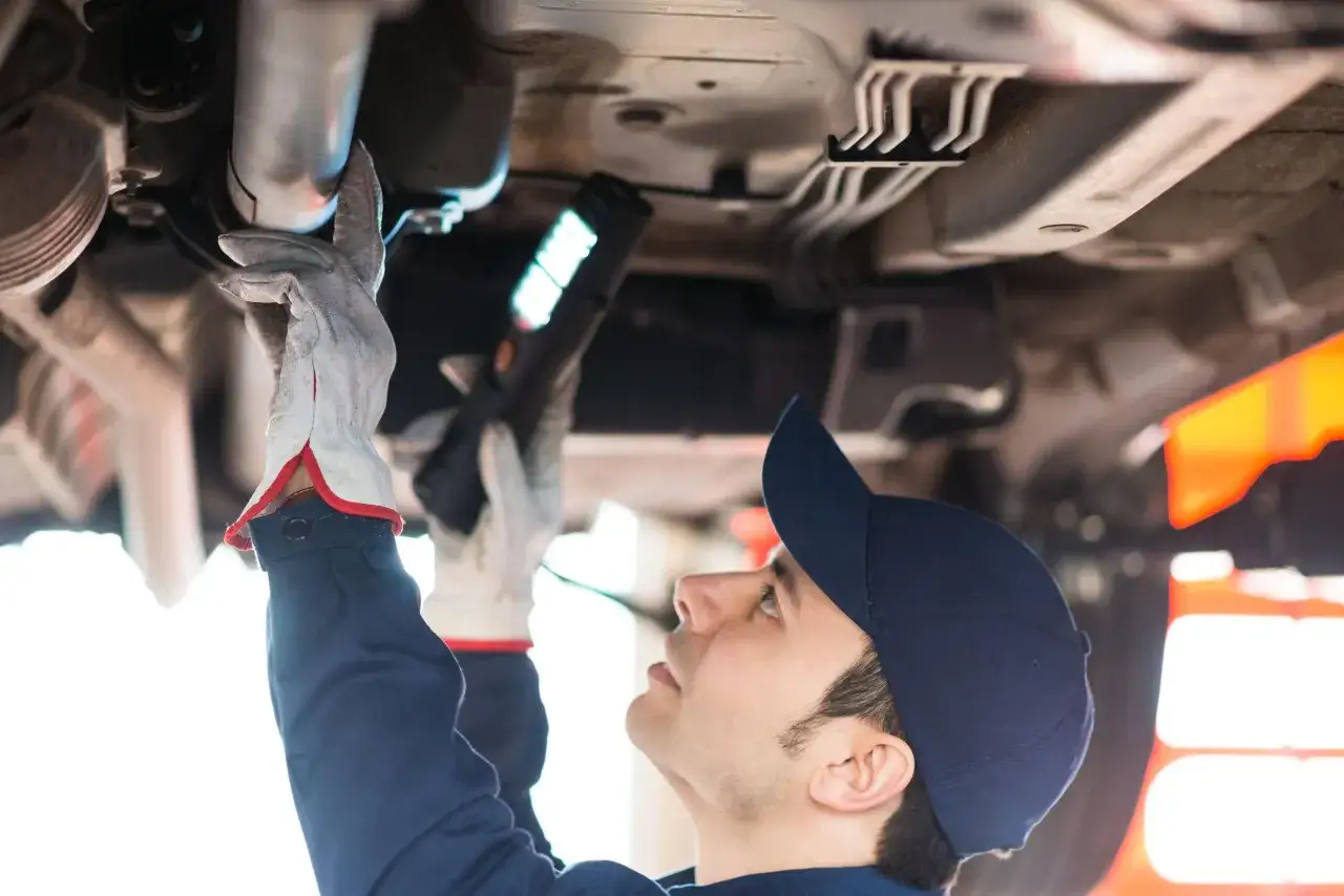 Meccanico con torcia esamina il sottoscocca di un'auto, essenziale per la revisione auto ibride.