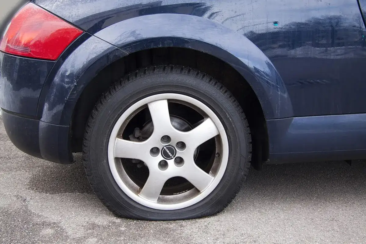 Ruota sgonfia di un'auto blu scuro. Il pneumatico è completamente a terra, appoggiato sul cerchione.