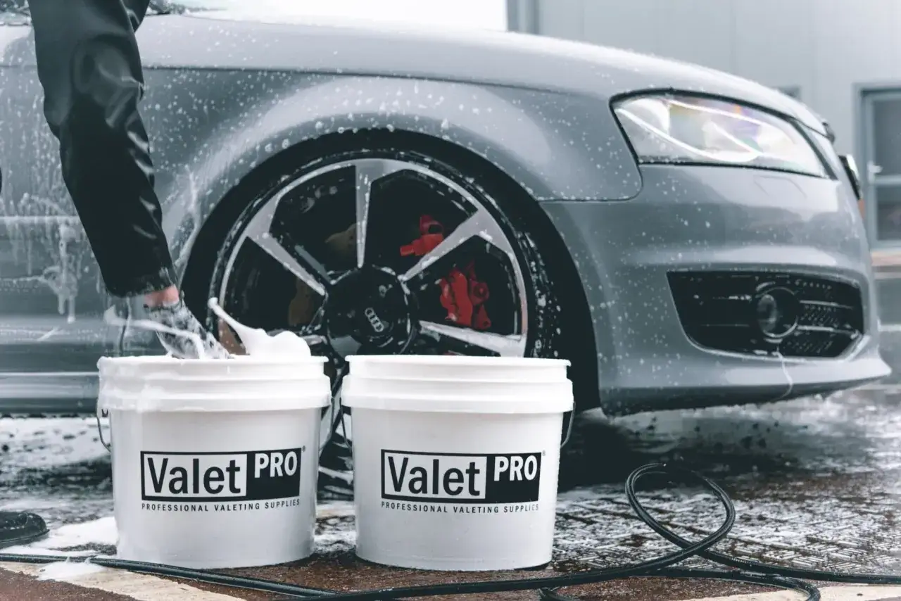 Persona che lava auto a casa con secchielli Valet PRO pieni di schiuma. Dettagli sui cerchi rossi e sul paraurti.