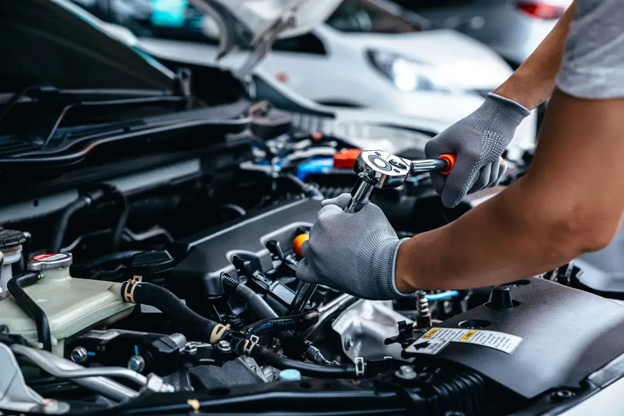 Mani guantate lavorano sul motore di una Mercedes A3, effettuando la manutenzione con una chiave a cricchetto.