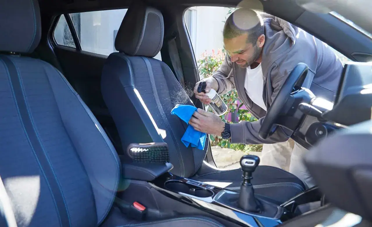Uomo che spruzza detergente sui sedili dell'auto e li pulisce con un panno blu.