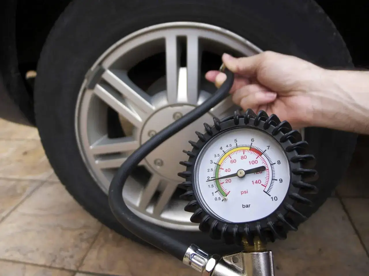 Controllo pressione gomme: il manometro indica 3 bar. La mano collega il tubo alla valvola.