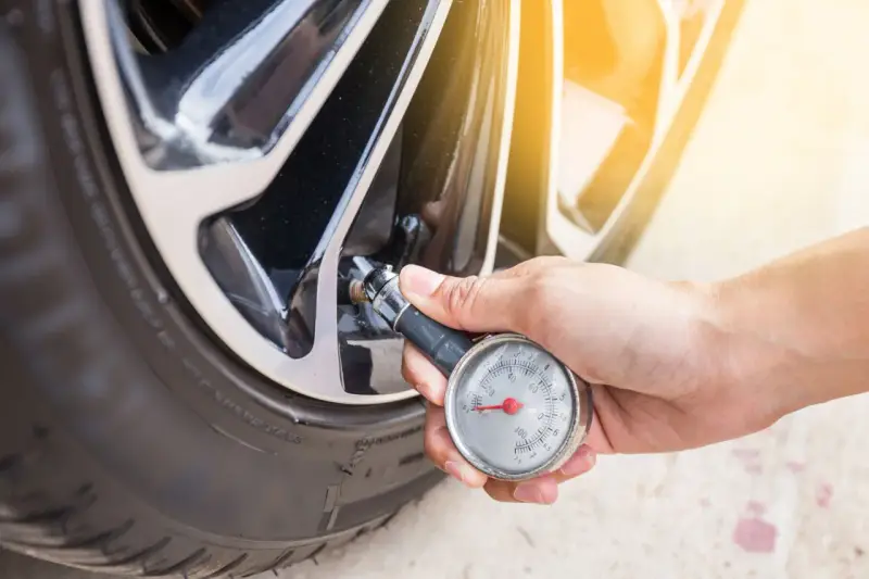 Controllo della pressione gomme auto con manometro. La mano tiene lo strumento collegato alla valvola del pneumatico.